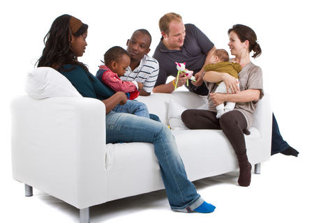 Young befriended multiracial families sitting on the couch and playing with their kids.
