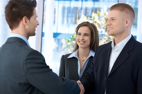 Businesspeople meeting in office, businessmen shaking hand, businesswoman smiling at introduction.
